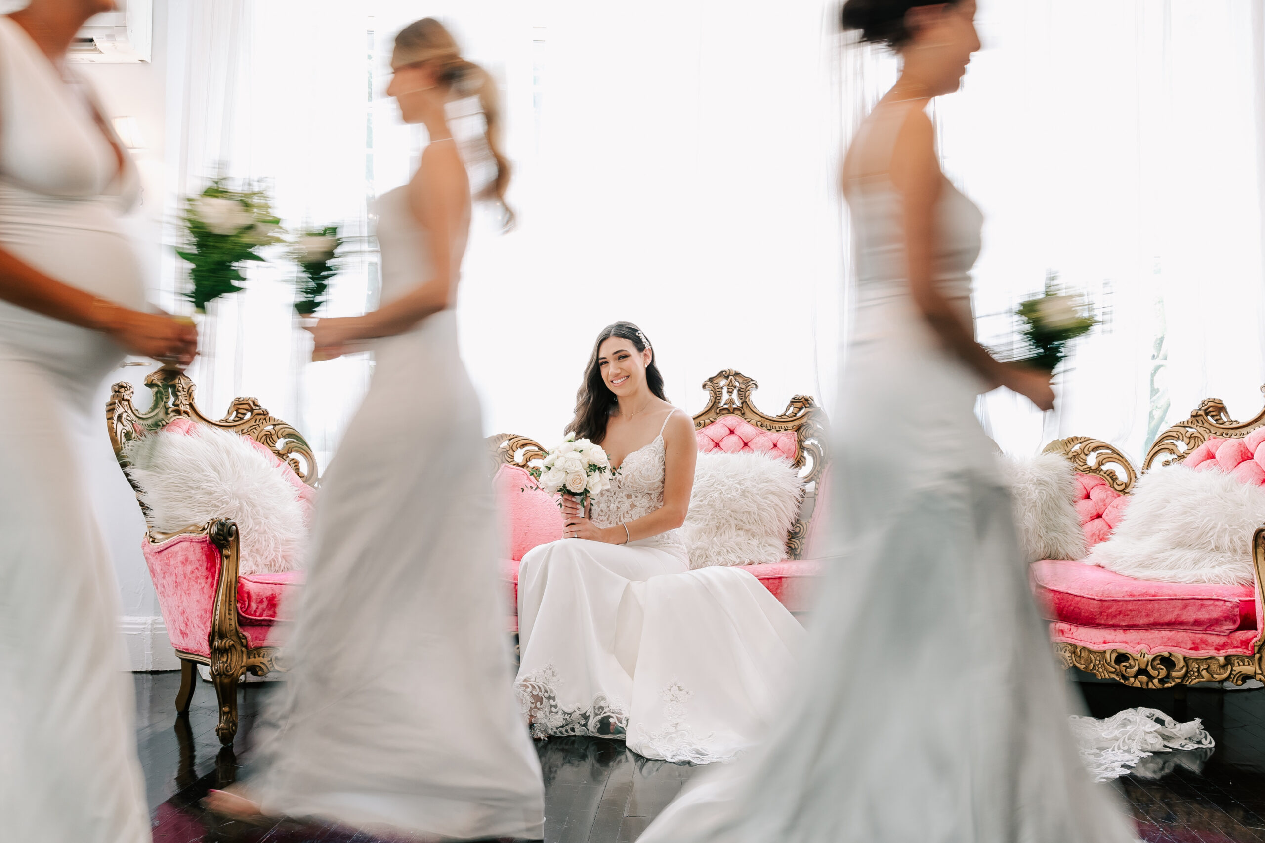 bride on pink couch with brides maids blurring past. 